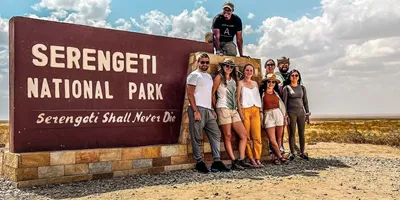 Group of travellers standing next to the entrance sign to the Serengeti National Park, Tanzania