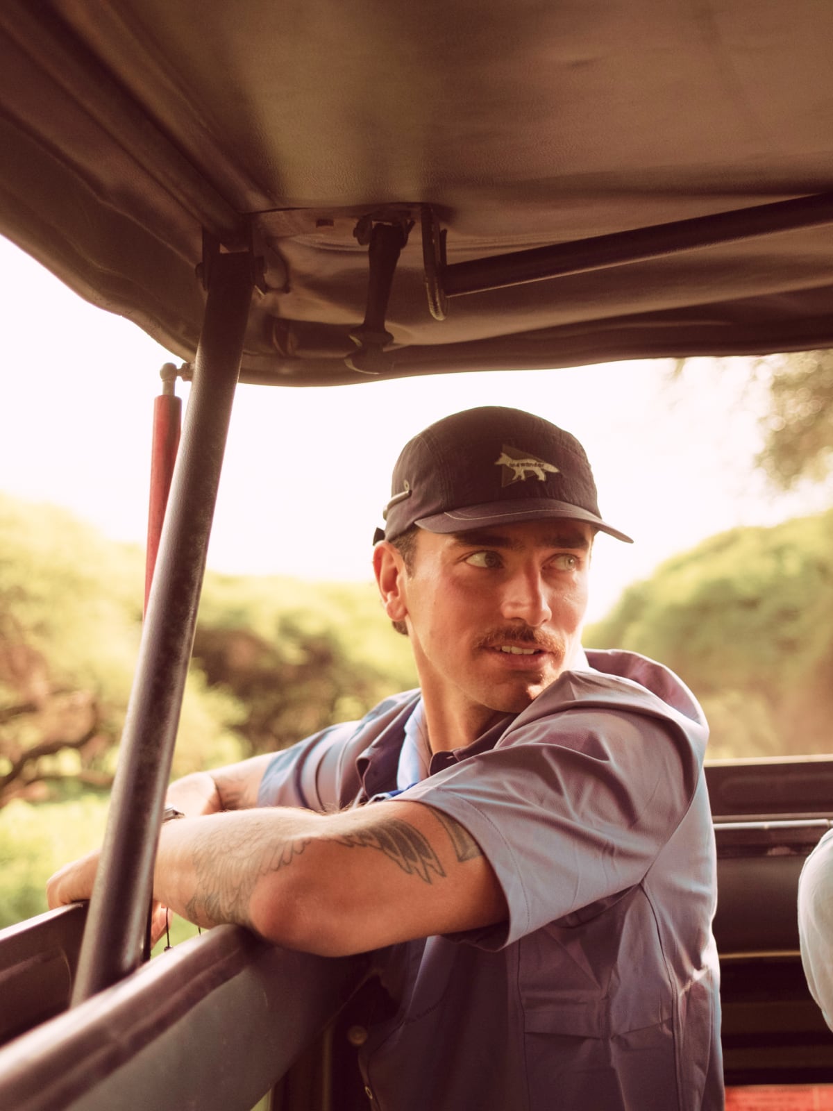 Safari guide looking back from an open-sided vehicle in the Tanzanian bush.