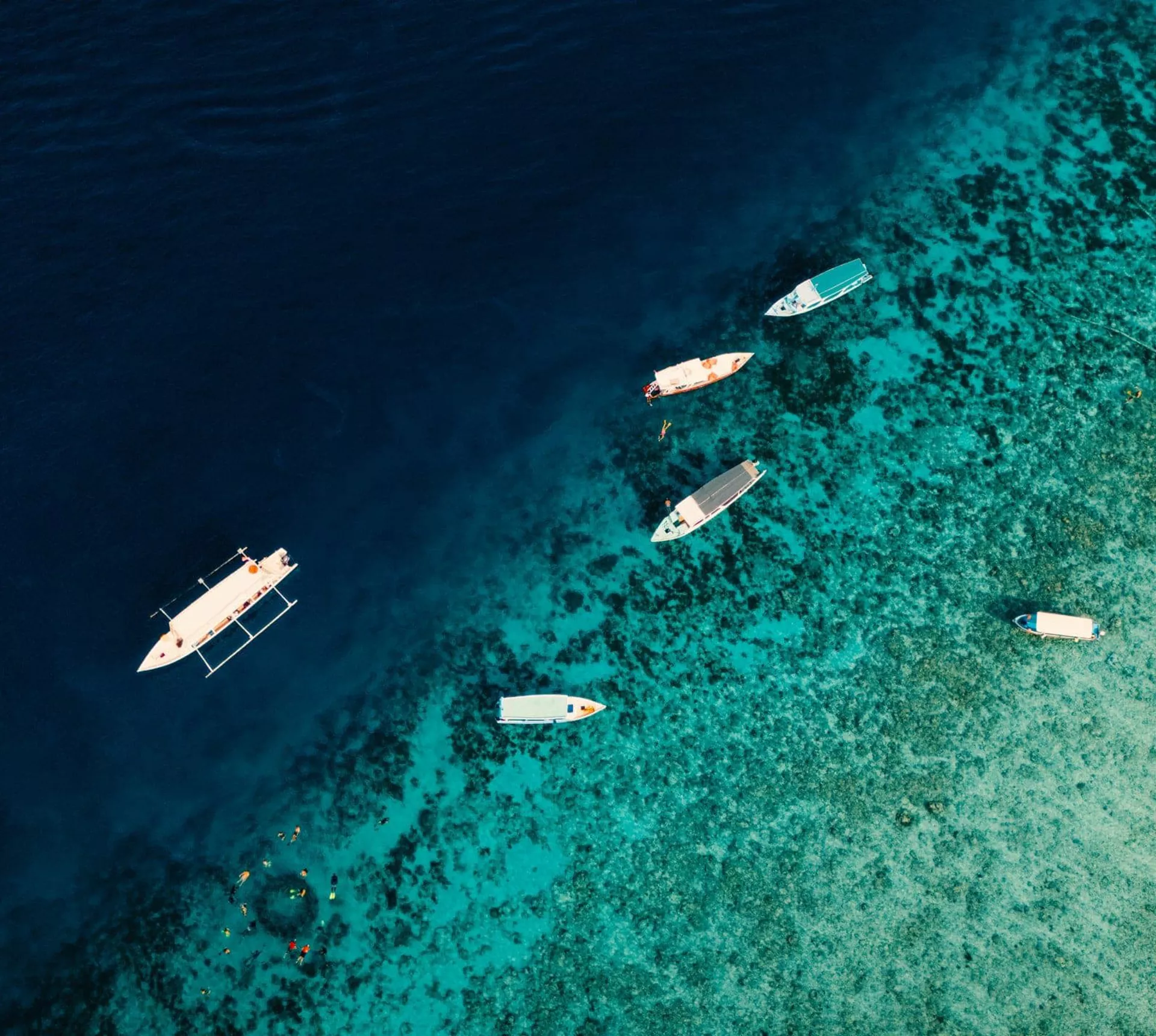 Aerial drone view of boats and snorkellers over a vivid turquoise coral reef drop-off in Bali Indonesia - Contiki Bali Island Hopping Tour