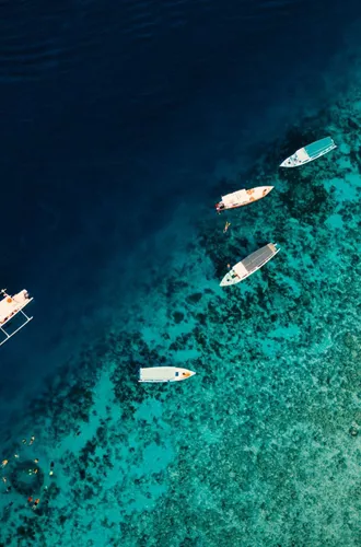 Aerial drone view of boats and snorkellers over a vivid turquoise coral reef drop-off in Bali Indonesia - Contiki Bali Island Hopping Tour