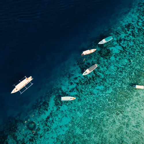 Aerial drone view of boats and snorkellers over a vivid turquoise coral reef drop-off in Bali Indonesia - Contiki Bali Island Hopping Tour
