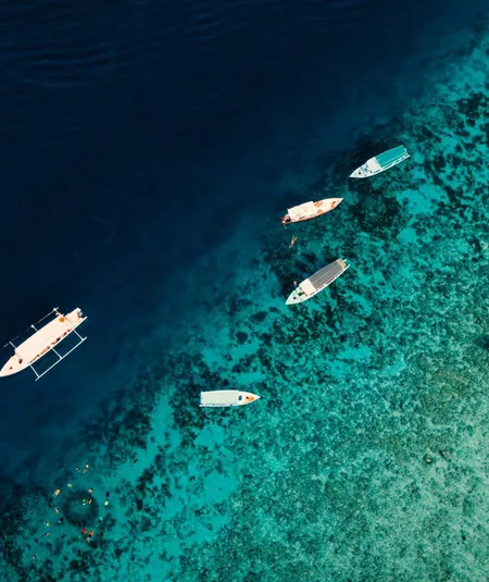 Aerial drone view of boats and snorkellers over a vivid turquoise coral reef drop-off in Bali Indonesia - Contiki Bali Island Hopping Tour