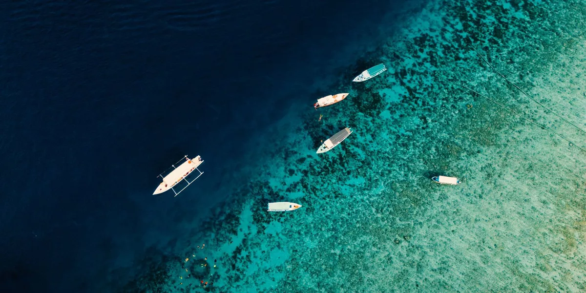 Aerial drone view of boats and snorkellers over a vivid turquoise coral reef drop-off in Bali Indonesia - Contiki Bali Island Hopping Tour