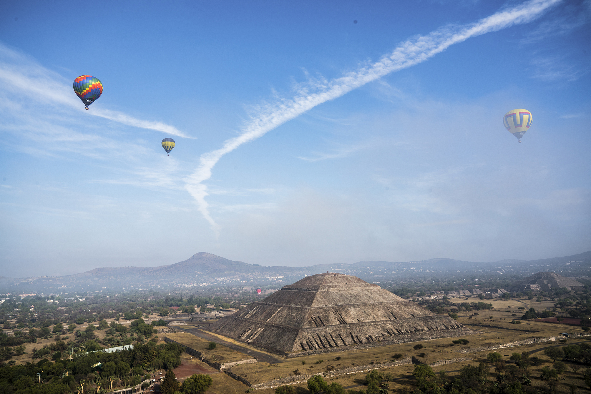 A landscape view of the Pyramind of the Sun, with hot air balloons floating in the sky, in Teotihuacan, Mexico