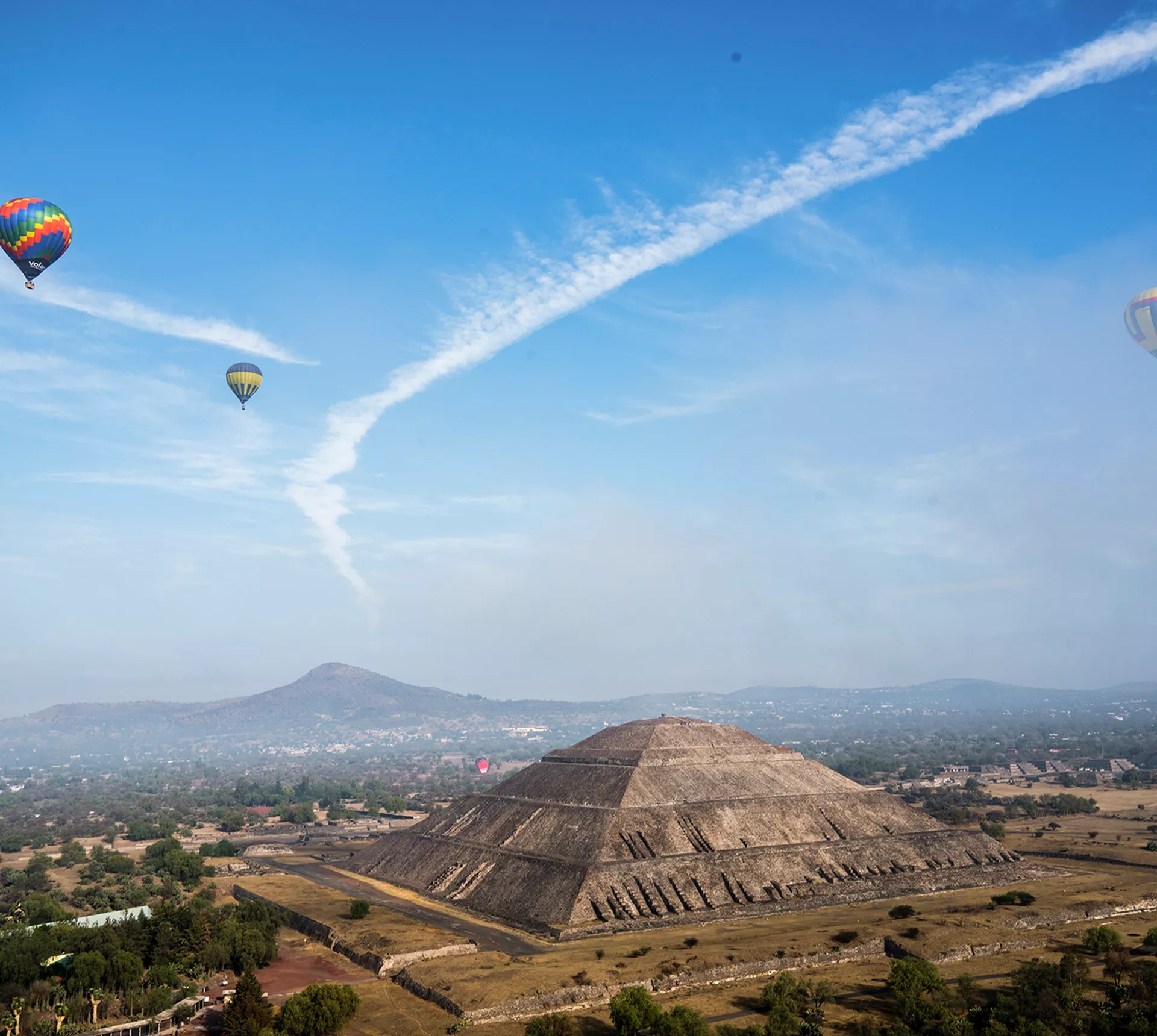 A landscape view of the Pyramind of the Sun, with hot air balloons floating in the sky, in Teotihuacan, Mexico