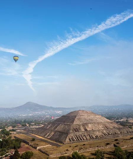 A landscape view of the Pyramind of the Sun, with hot air balloons floating in the sky, in Teotihuacan, Mexico