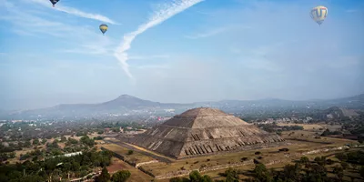 A landscape view of the Pyramind of the Sun, with hot air balloons floating in the sky, in Teotihuacan, Mexico