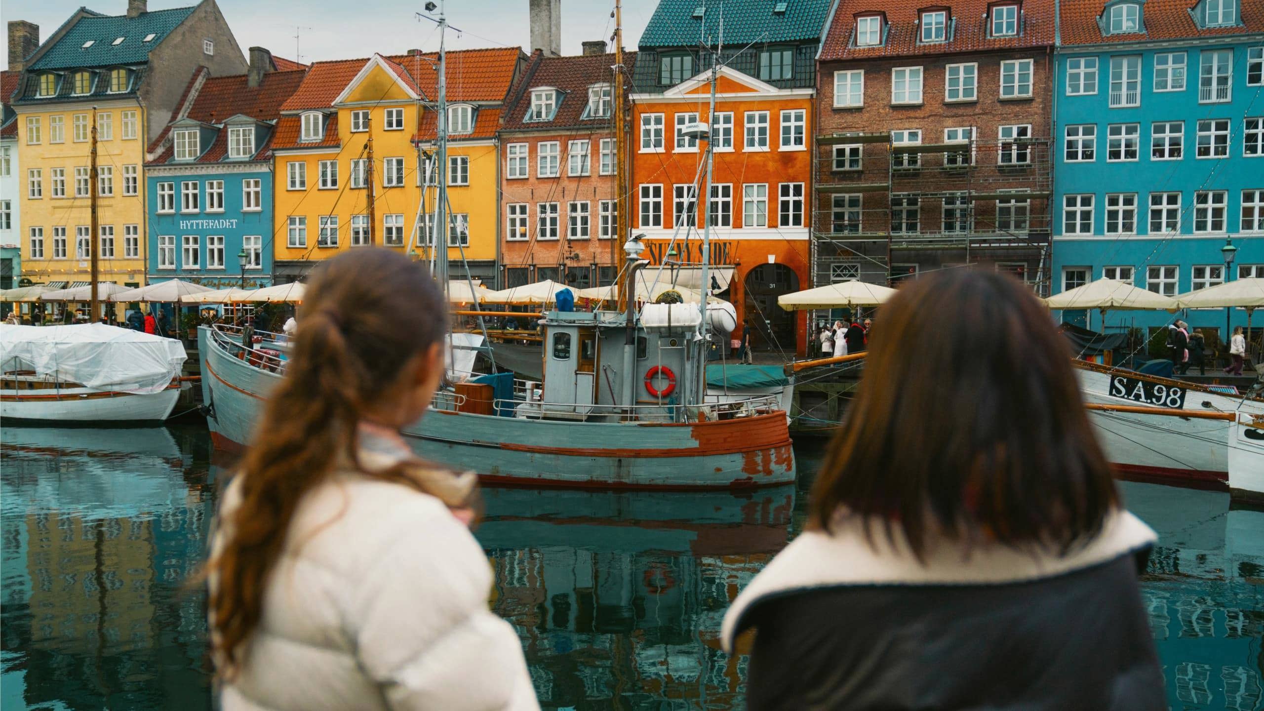 Travellers admire the colourful waterfront buildings and historic boats of Nyhavn in Copenhagen on the Contiki Best of Scandinavia Tour
