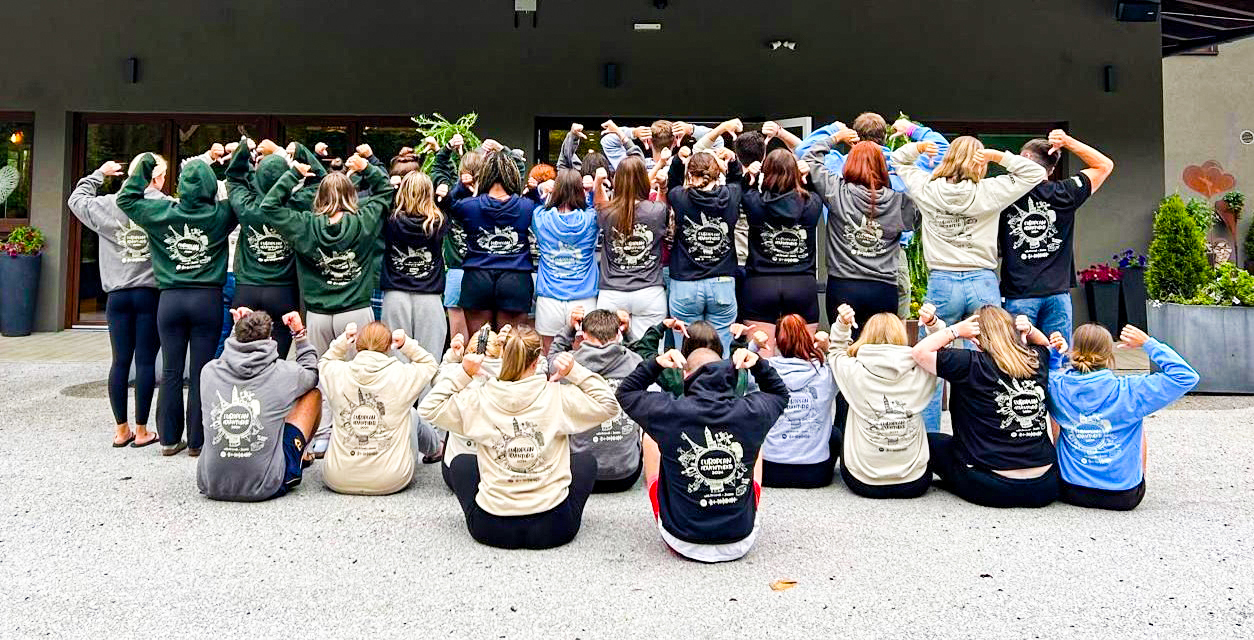 A large group of travellers facing away from the camera, showing the design on the back of their hoodie or t shirt
