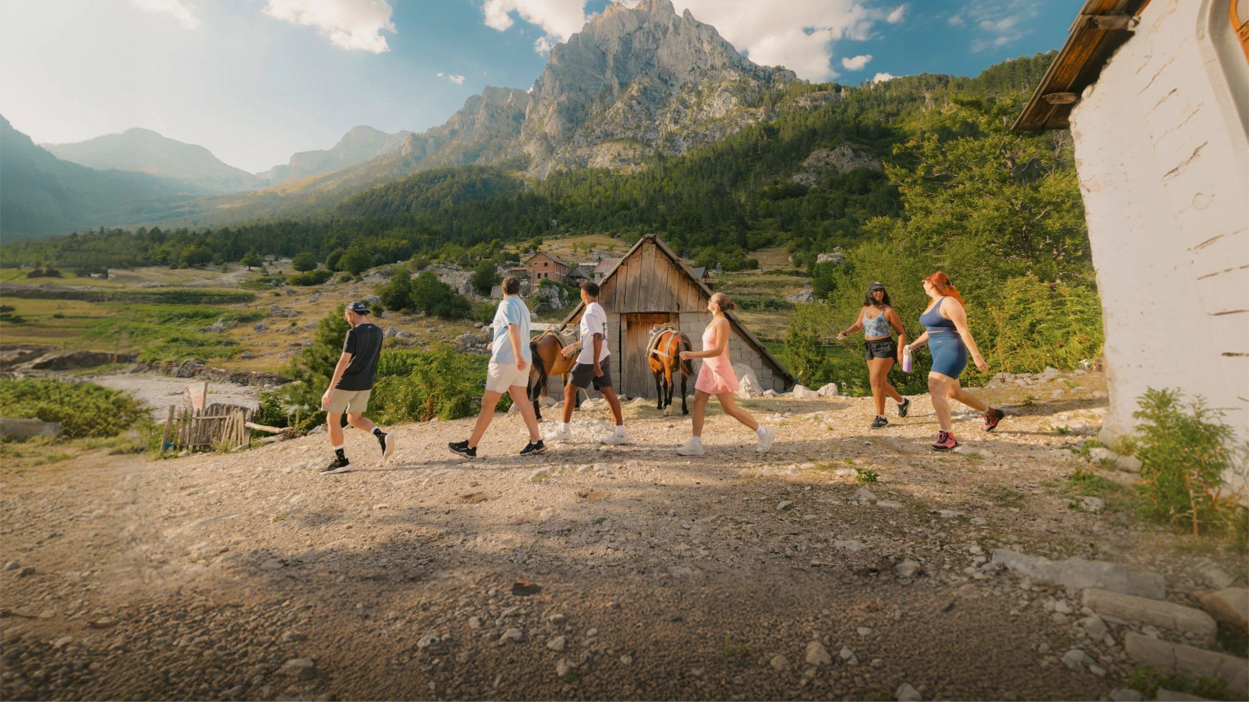 Travellers walk through a mountain village surrounded by rugged peaks and forest on the Contiki Albania: Beaches & Mountains Tour