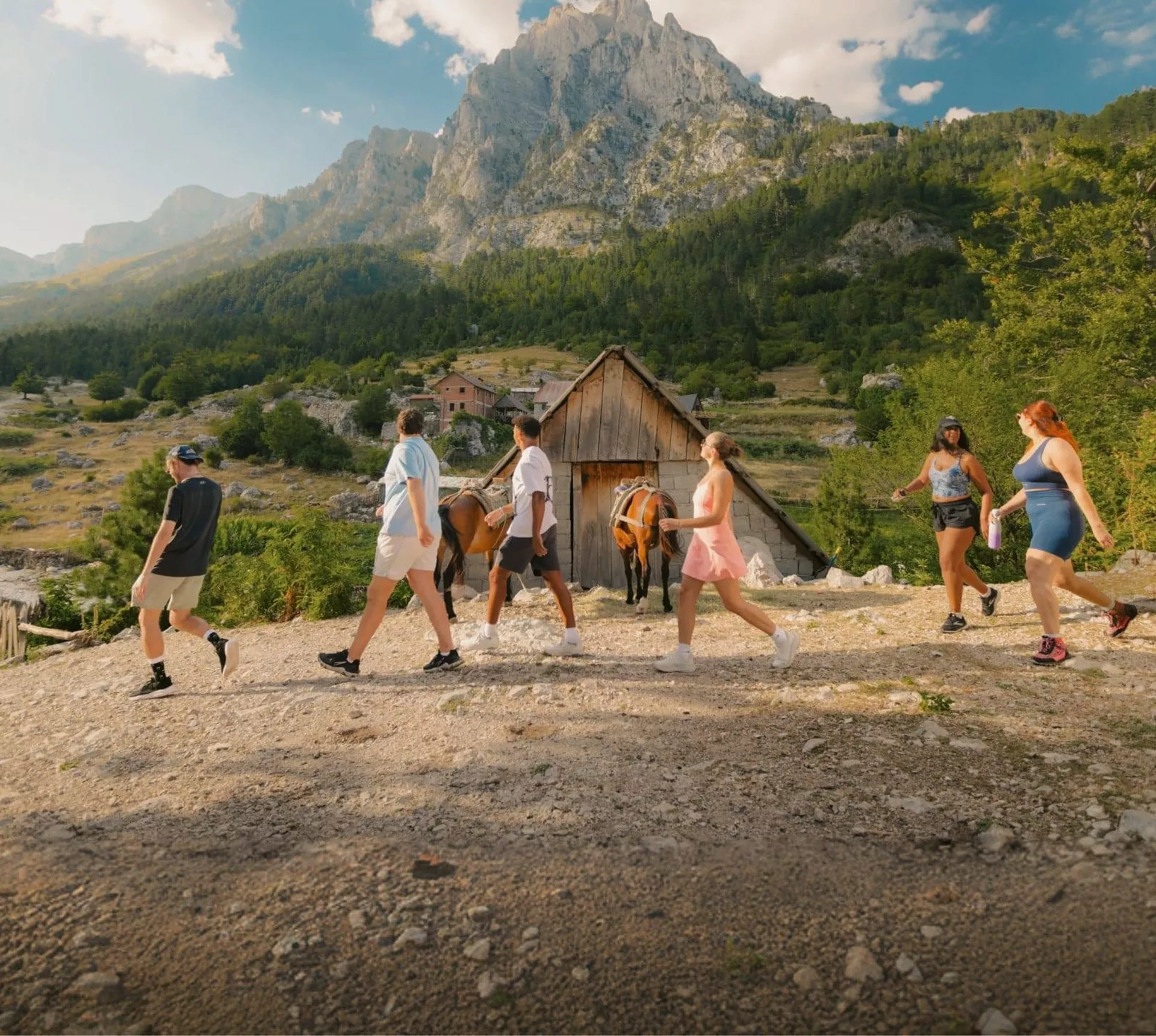 Travellers walk through a mountain village surrounded by rugged peaks and forest on the Contiki Albania: Beaches & Mountains Tour