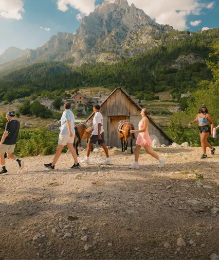Travellers walk through a mountain village surrounded by rugged peaks and forest on the Contiki Albania: Beaches & Mountains Tour