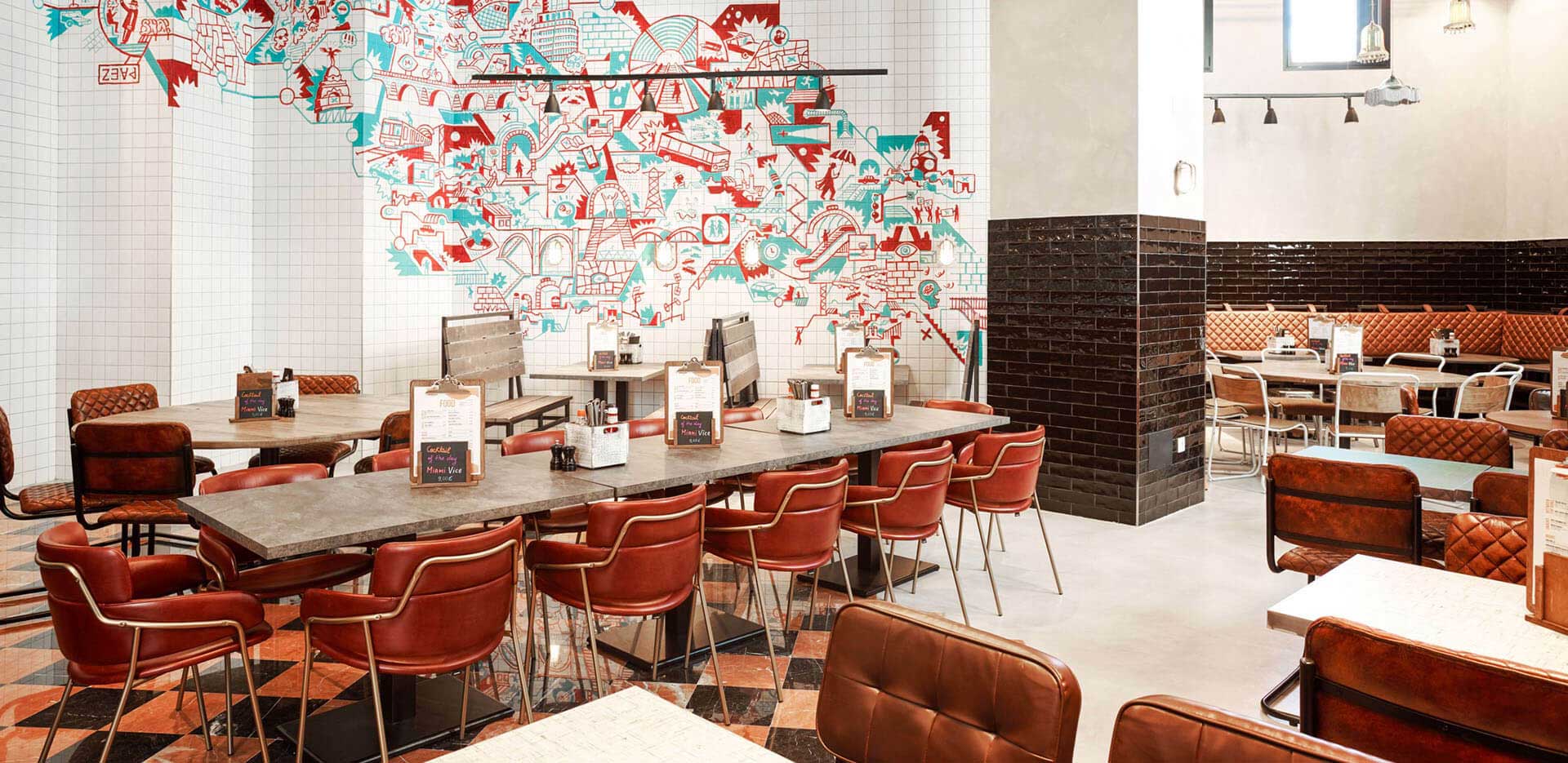 Generator Hostel dining room with long tables, red chairs and wall mosaic 