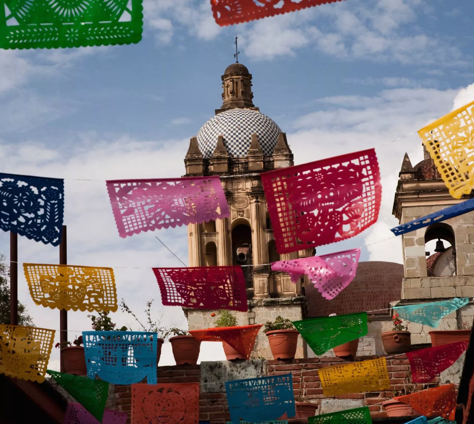Colourful papel picado banners hanging above a colonial Mexican street with a baroque church dome and bell tower in Oaxaca Mexico - Contiki Mexico Tour