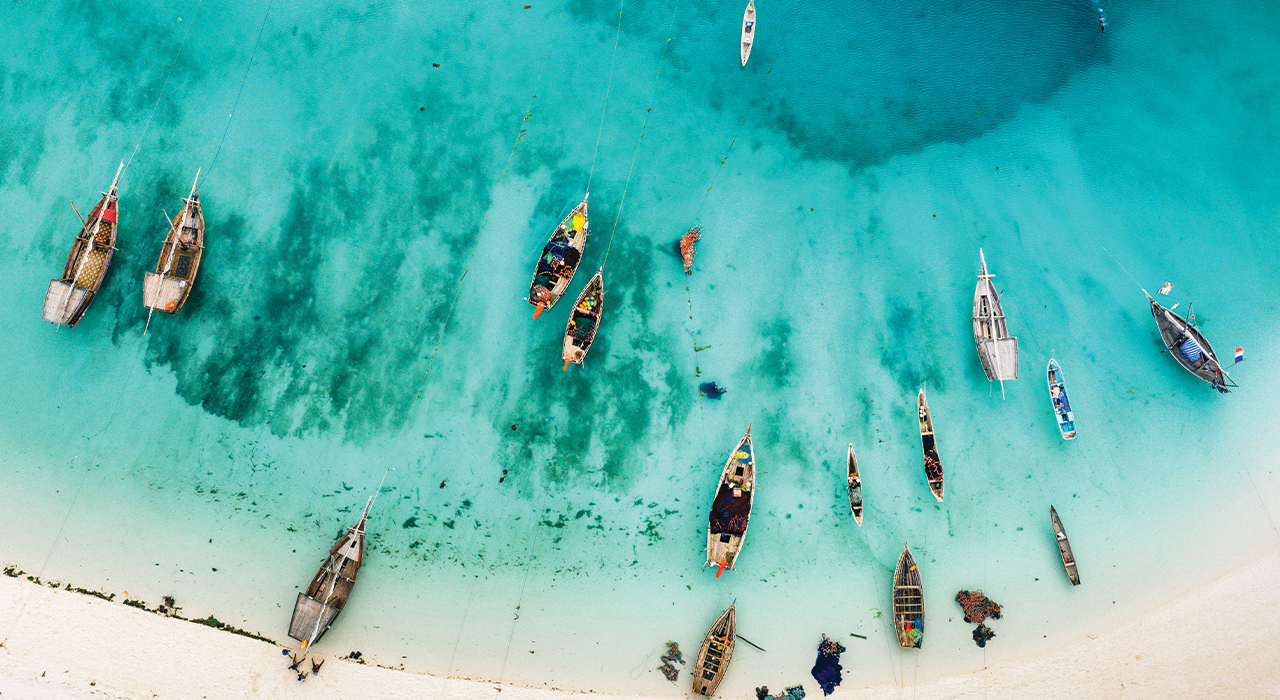 Aerial View Of Traditional Dhow Boats On Turquoise Water Near White Sand Beach In Zanzibar