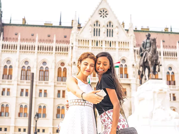 Two Friends Smiling Taking A Selfie Landmark In The Background