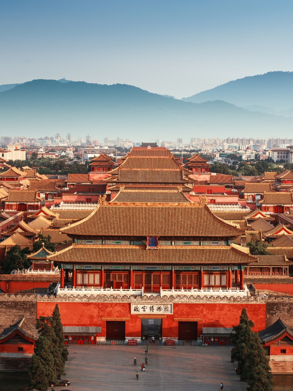 View over the Forbidden City in Beijing, China, with traditional palace rooftops and mountains in the background.