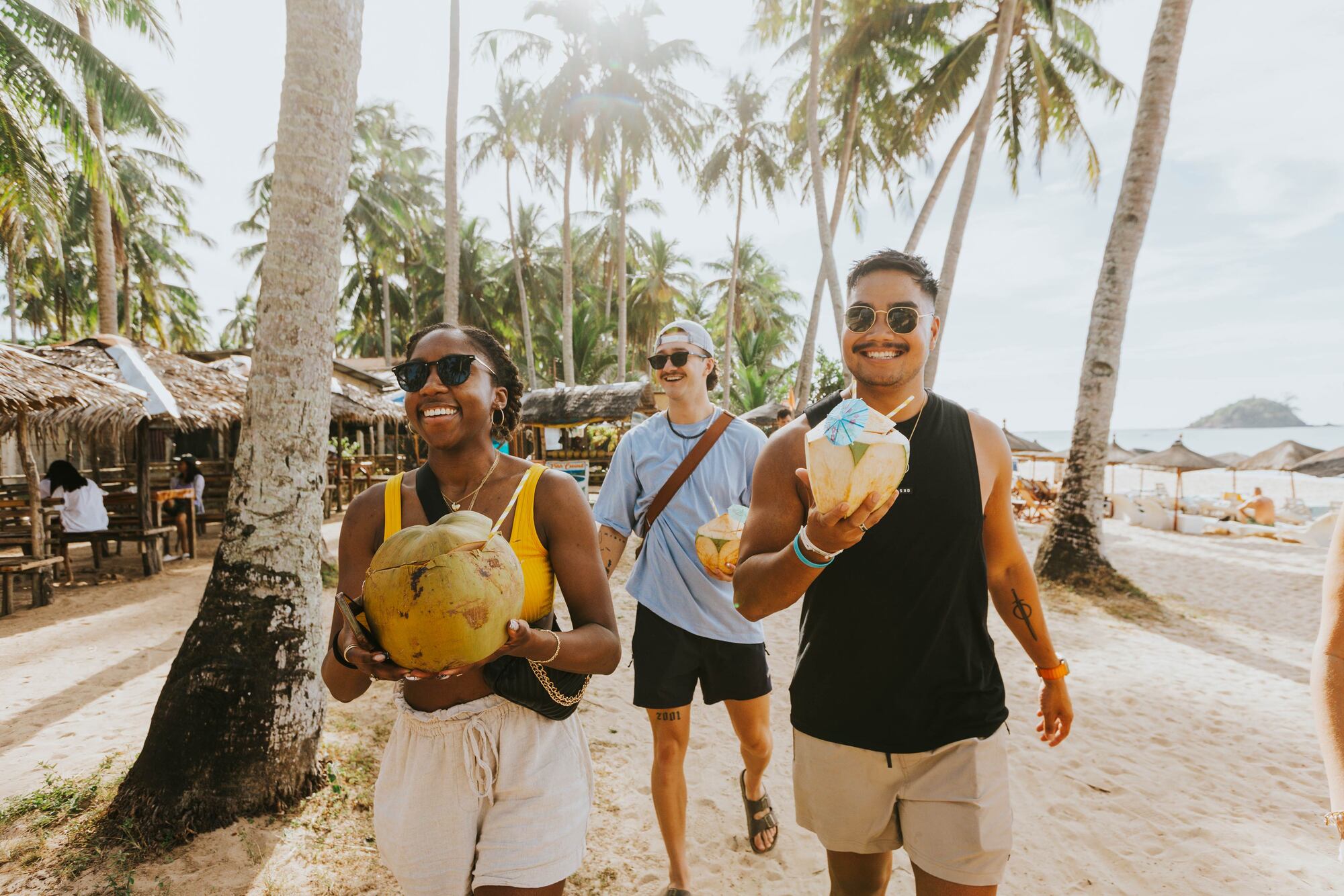People walking down a beach holding coconuts