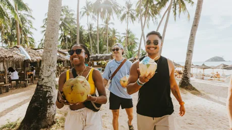 People walking down a beach holding coconuts
