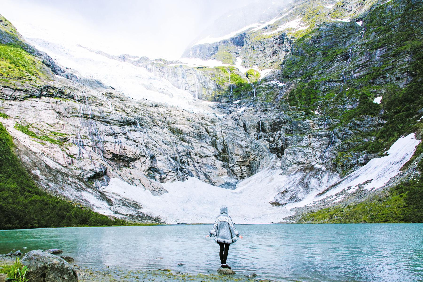 Woman in blue jacket standing in front of lake formed by Boyabreen Glacier in Norway