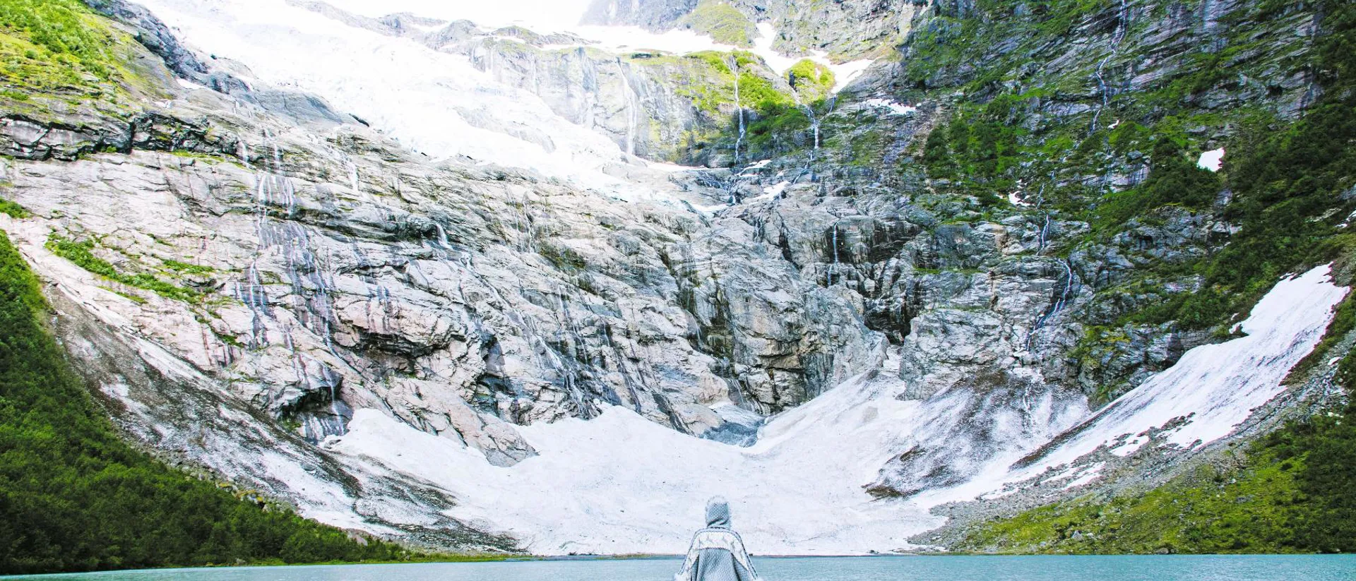 Woman in blue jacket standing in front of lake formed by Boyabreen Glacier in Norway