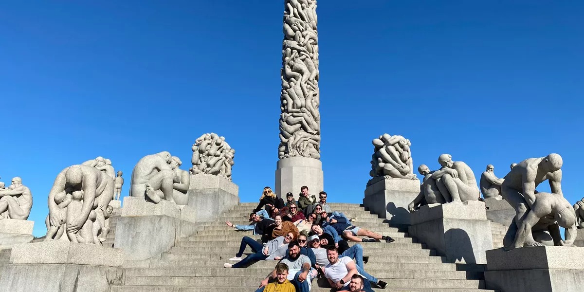 A large group of friends visiting a landmark on a sunny day in Norway.