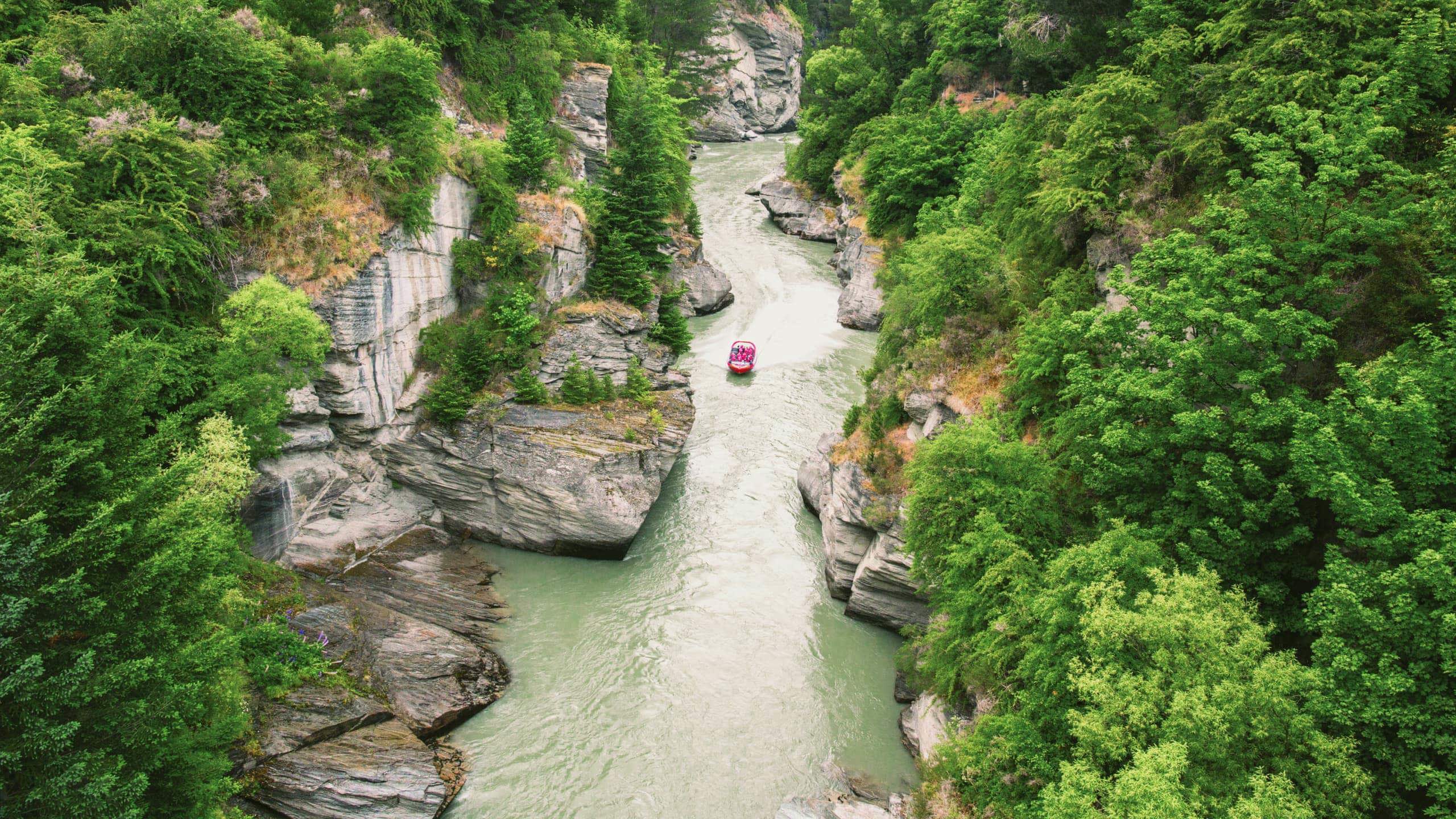 Red jet boat navigating the narrow Shotover River Canyon gorge near Queenstown New Zealand - Contiki NZ Tour