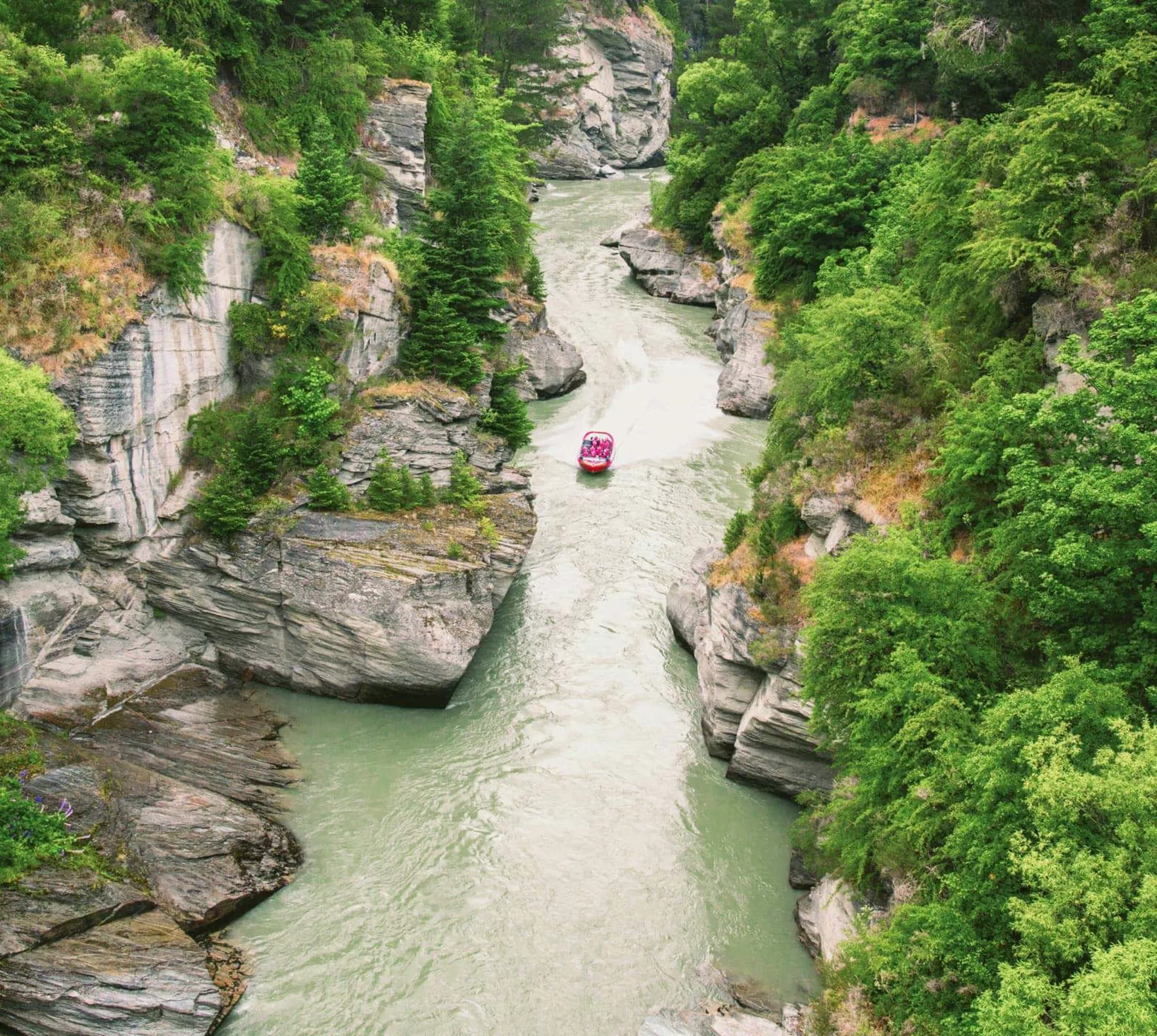 Red jet boat navigating the narrow Shotover River Canyon gorge near Queenstown New Zealand - Contiki NZ Tour