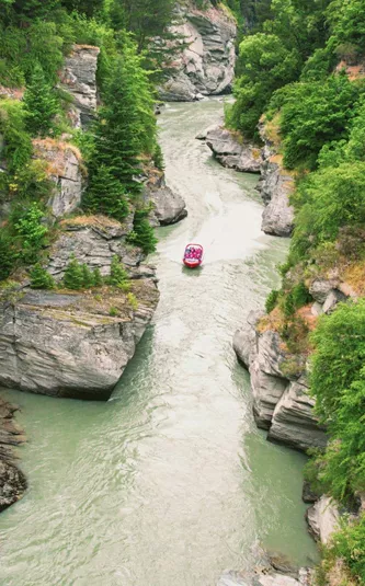 Red jet boat navigating the narrow Shotover River Canyon gorge near Queenstown New Zealand - Contiki NZ Tour
