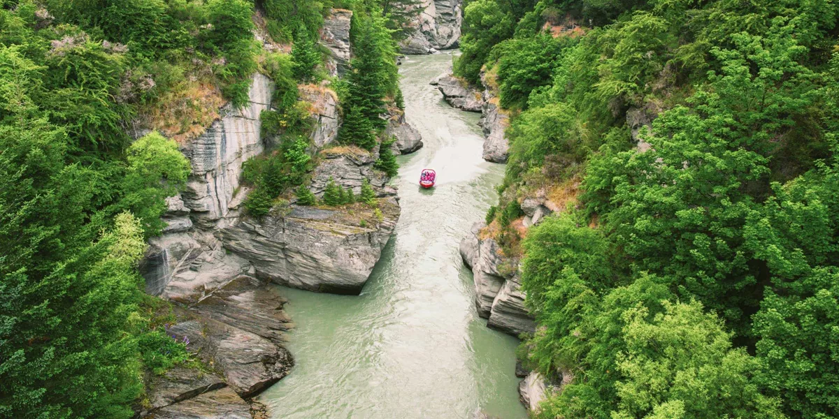 Red jet boat navigating the narrow Shotover River Canyon gorge near Queenstown New Zealand - Contiki NZ Tour