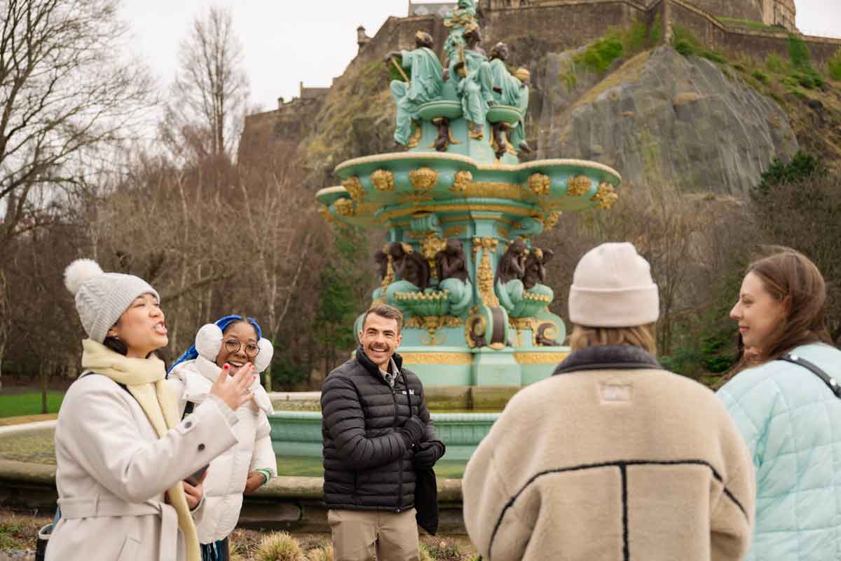 A group of people chatting and laughing near a decorative fountain in a park