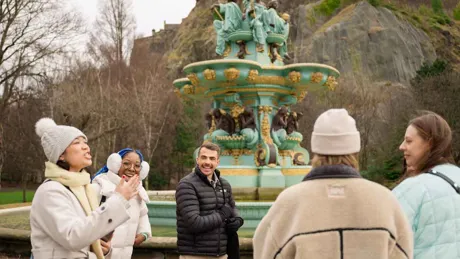 A group of people chatting and laughing near a decorative fountain in a park