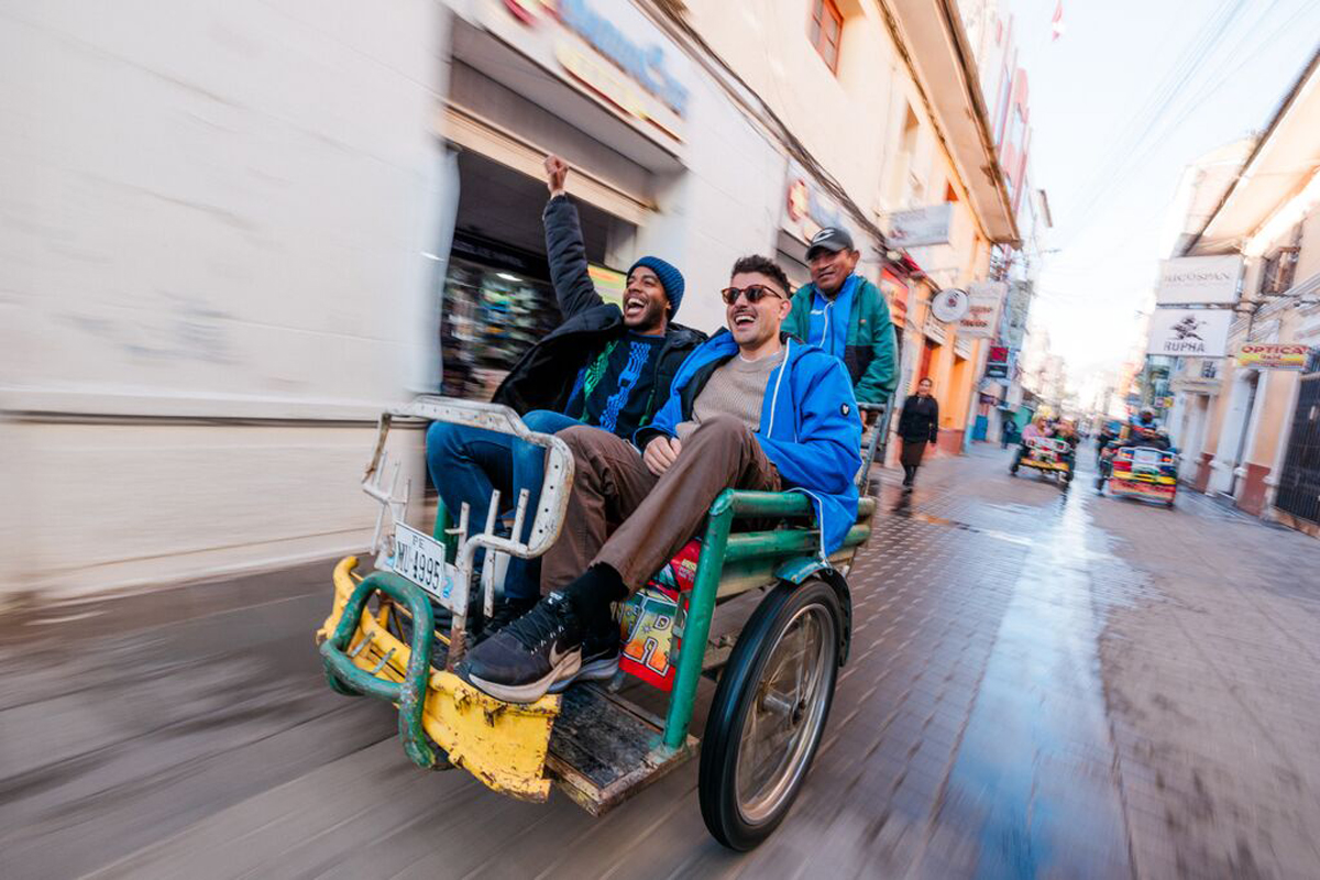 A couple of men riding on the back of a green cart