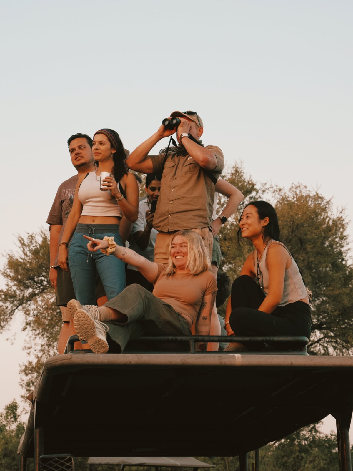 Group of travellers spotting wildlife with binoculars from atop a safari vehicle in Botswana