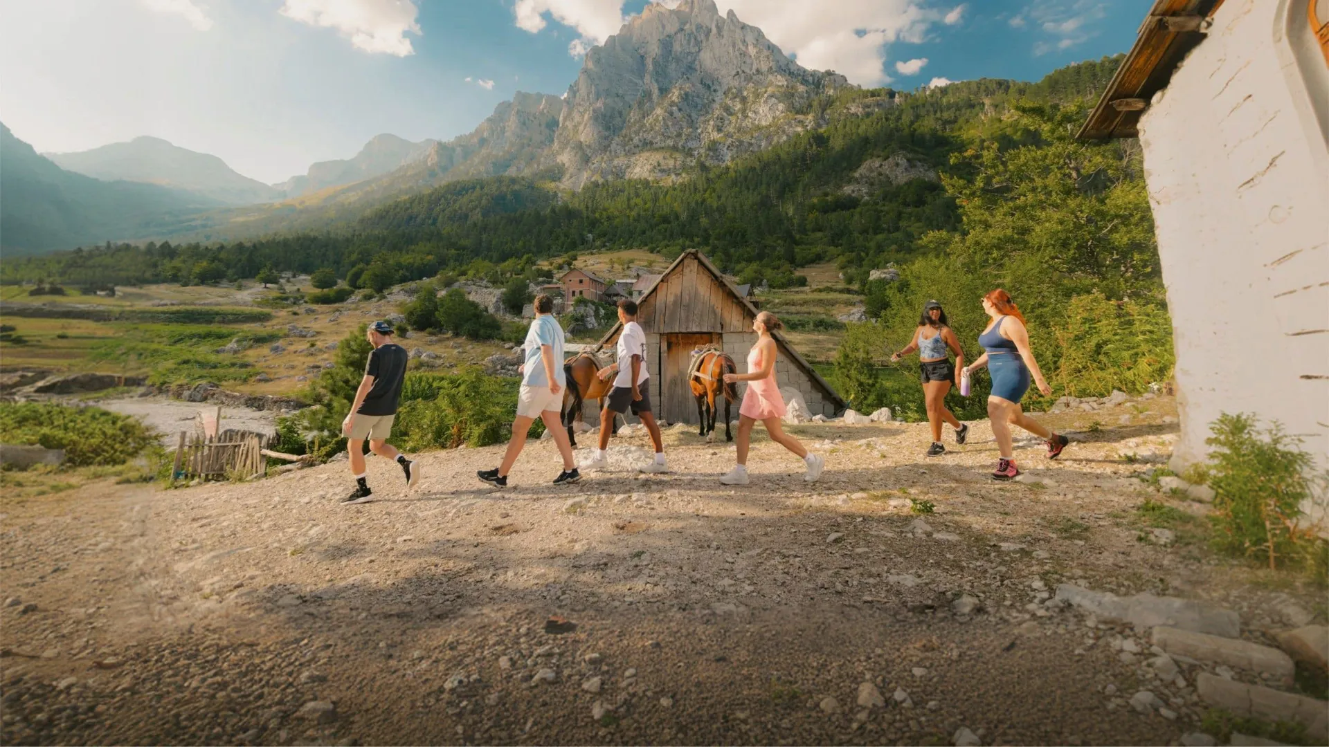 Travellers walk through a mountain village surrounded by rugged peaks and forest on the Contiki Albania: Beaches & Mountains Tour