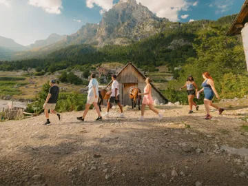 Travellers walk through a mountain village surrounded by rugged peaks and forest on the Contiki Albania: Beaches & Mountains Tour