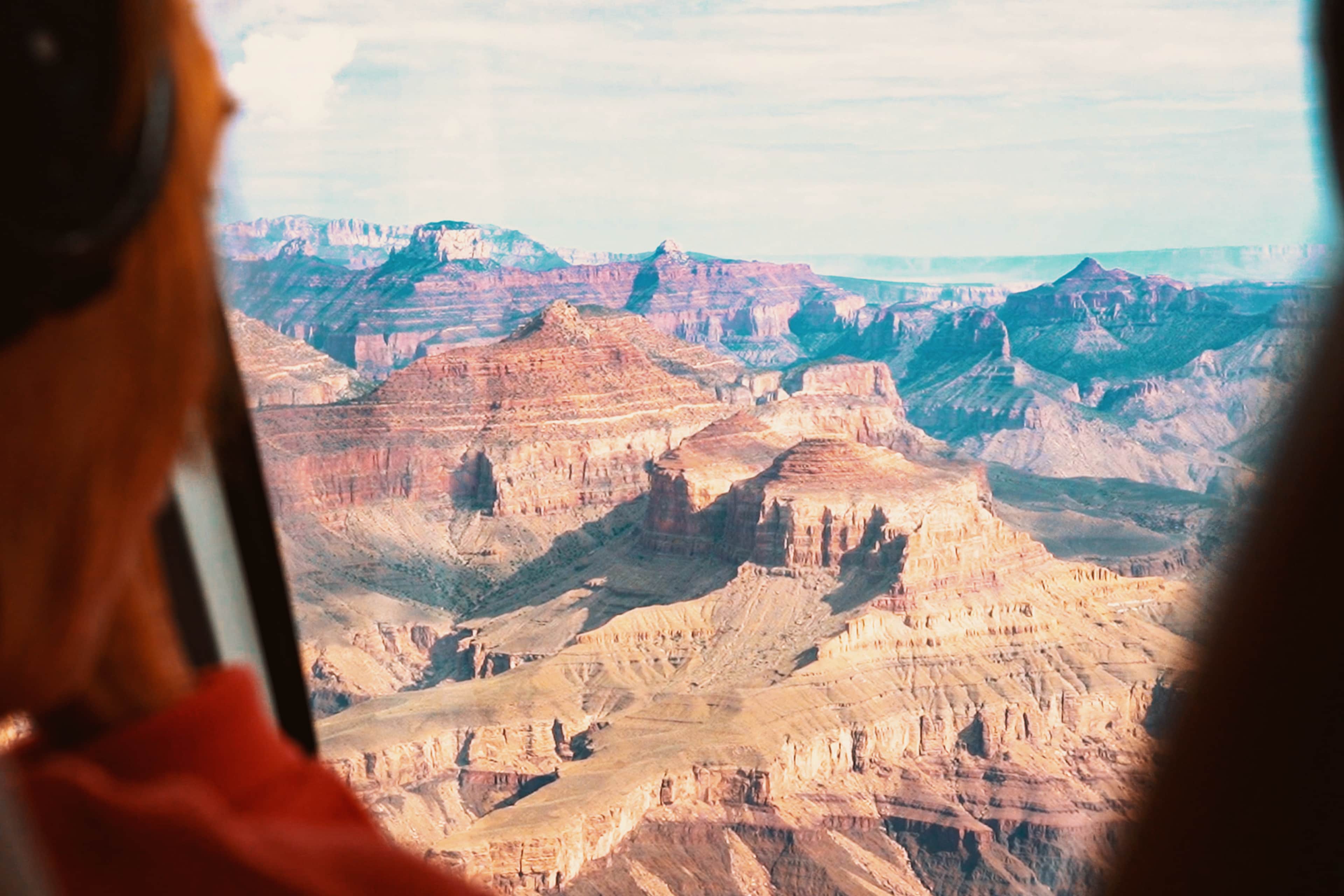Traveller wearing headphones taking in aerial views of the Grand Canyon's layered rock formations from a helicopter.