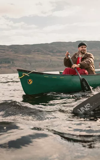 Contiki Travellers explore the Scottish Highlands by canoe, paddling across a tranquil loch with rolling hills in the background - Best of England & Scotland Summer Tour