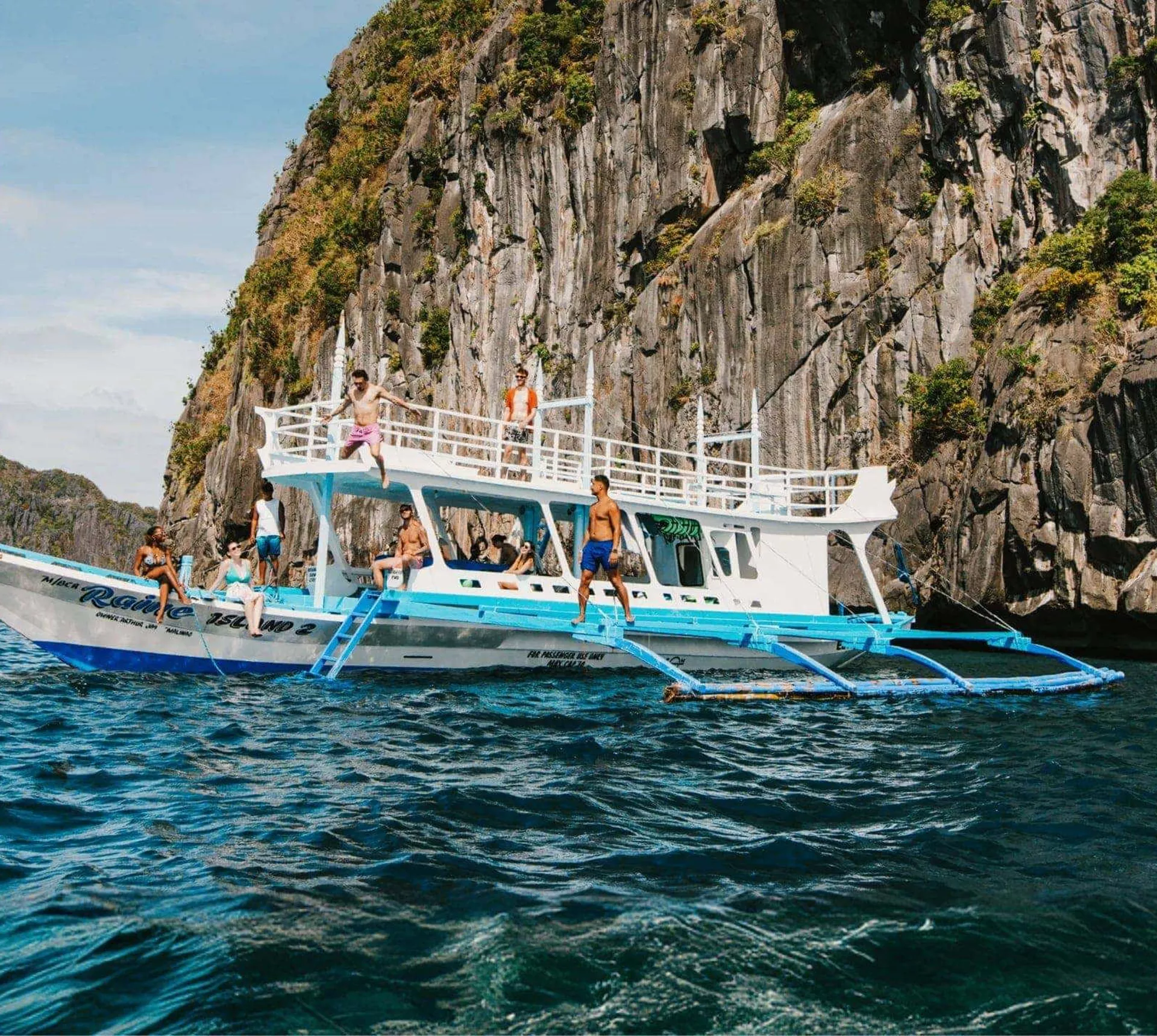 Group of young travellers jumping off a traditional Filipino bangka boat into the sea surrounded by dramatic limestone cliffs in El Nido Palawan Philippines - Contiki Philippines island hopping Tour