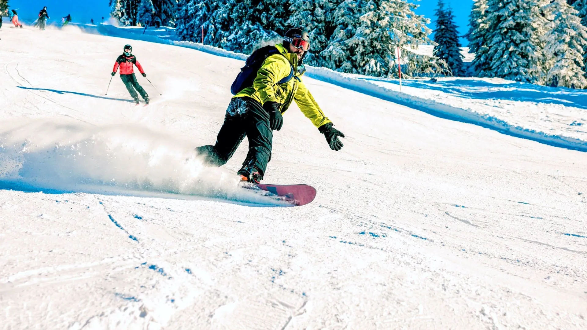 A snowboarder carves down a snowy slope in the Austrian Alps, with skiers following behind on a clear winter day