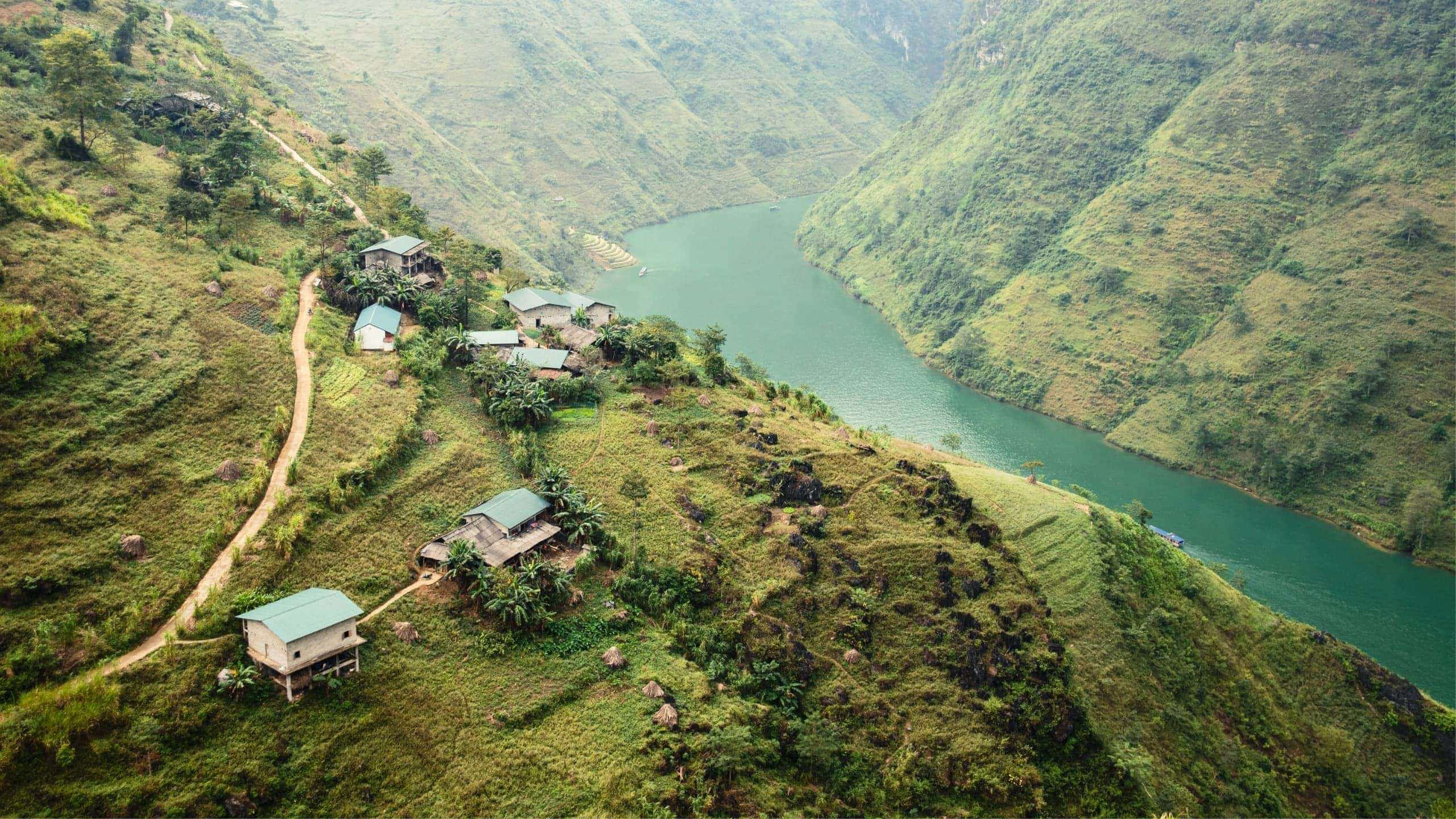 A winding emerald river curves through the mountains of northern Vietnam, with small rural villages and terraced hillsides overlooking the Ha Giang Loop - Northern Vietnam Tour