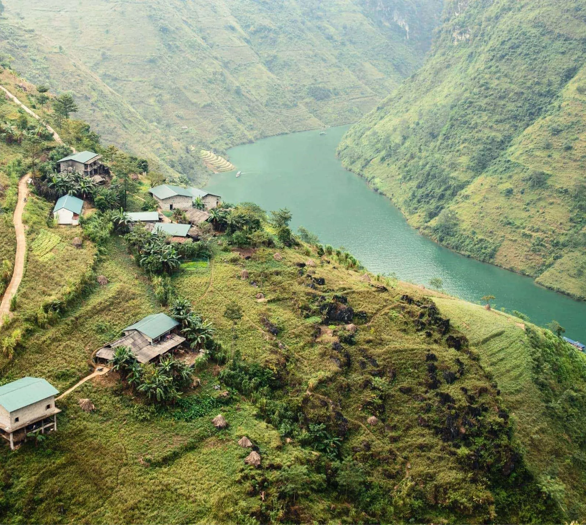 A winding emerald river curves through the mountains of northern Vietnam, with small rural villages and terraced hillsides overlooking the Ha Giang Loop - Northern Vietnam Tour