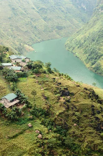 A winding emerald river curves through the mountains of northern Vietnam, with small rural villages and terraced hillsides overlooking the Ha Giang Loop - Northern Vietnam Tour