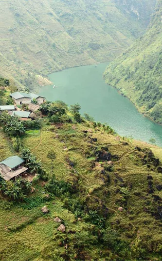 A winding emerald river curves through the mountains of northern Vietnam, with small rural villages and terraced hillsides overlooking the Ha Giang Loop - Northern Vietnam Tour