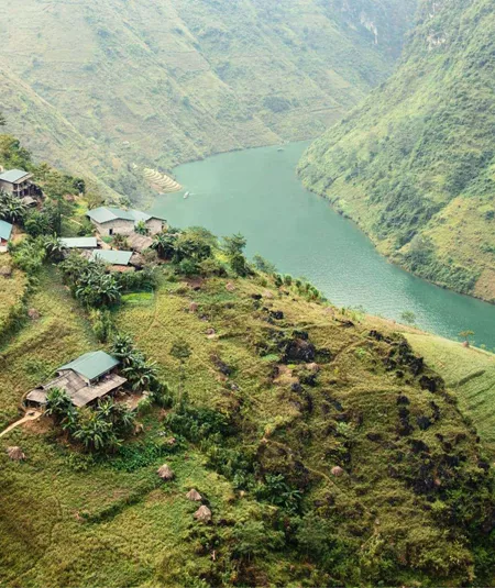 A winding emerald river curves through the mountains of northern Vietnam, with small rural villages and terraced hillsides overlooking the Ha Giang Loop - Northern Vietnam Tour