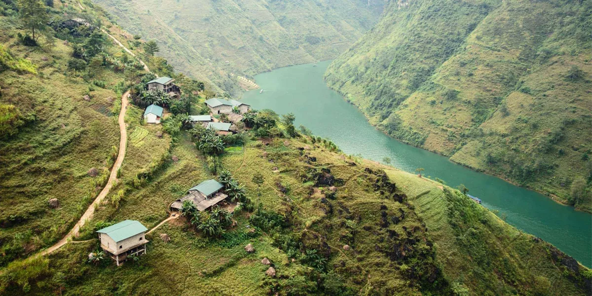 A winding emerald river curves through the mountains of northern Vietnam, with small rural villages and terraced hillsides overlooking the Ha Giang Loop - Northern Vietnam Tour