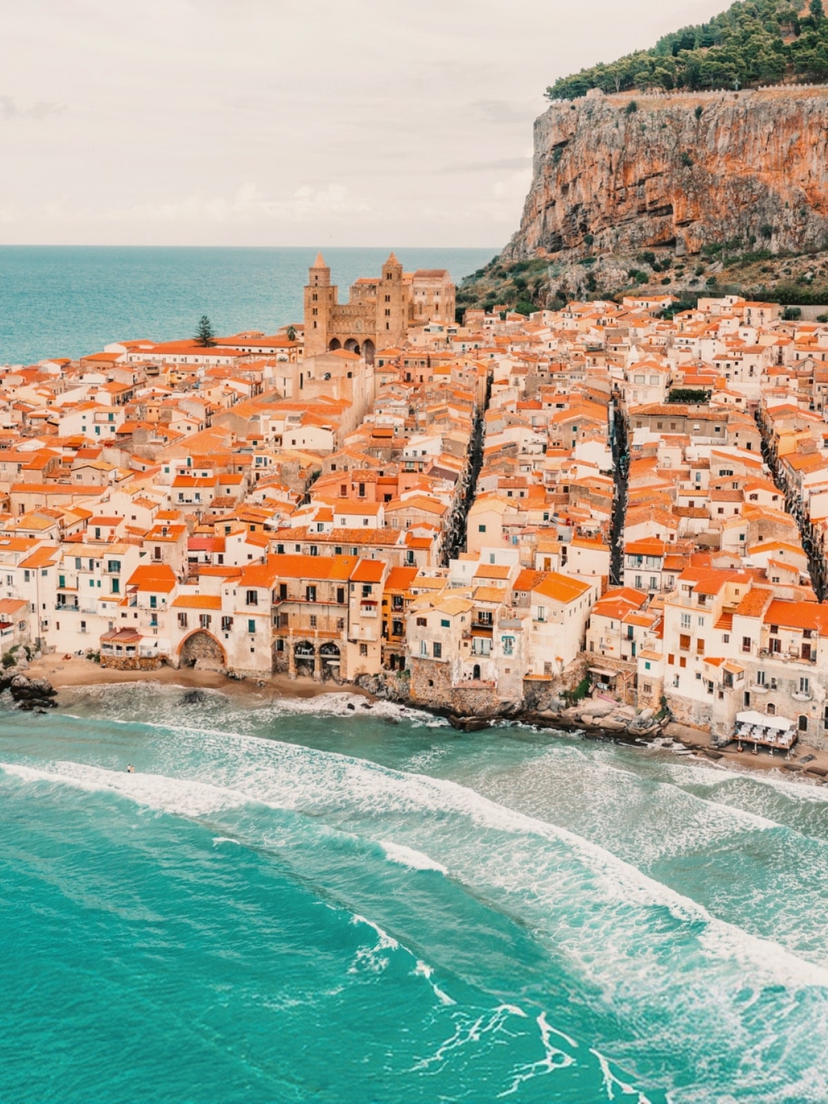 Aerial view of Cefalù's historic old town and turquoise coastline in Sicily, Italy.