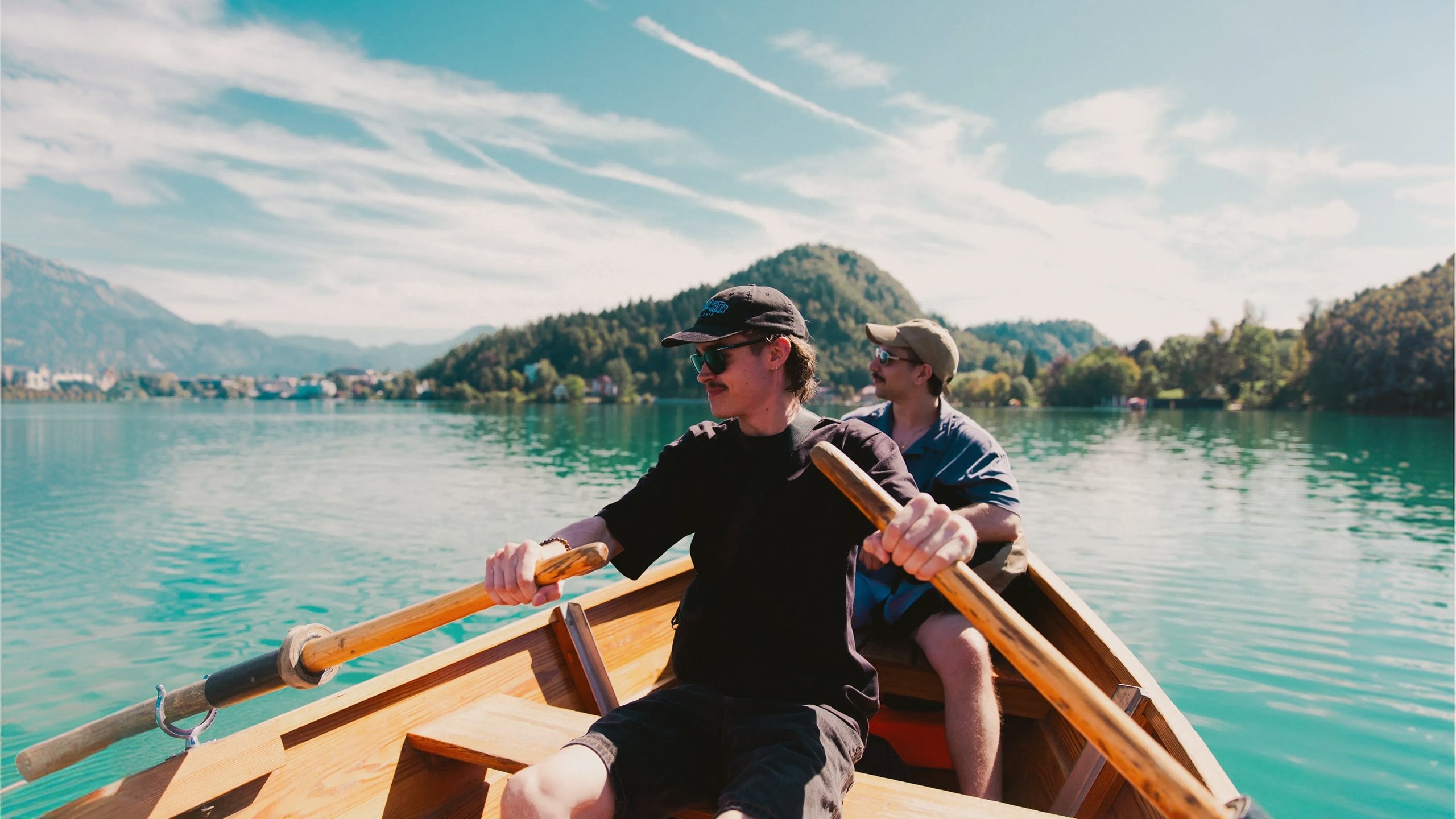 Travellers take in stunning mountain views while rowing across an emerald lake on the Contiki Budapest to Dubrovnik Tour