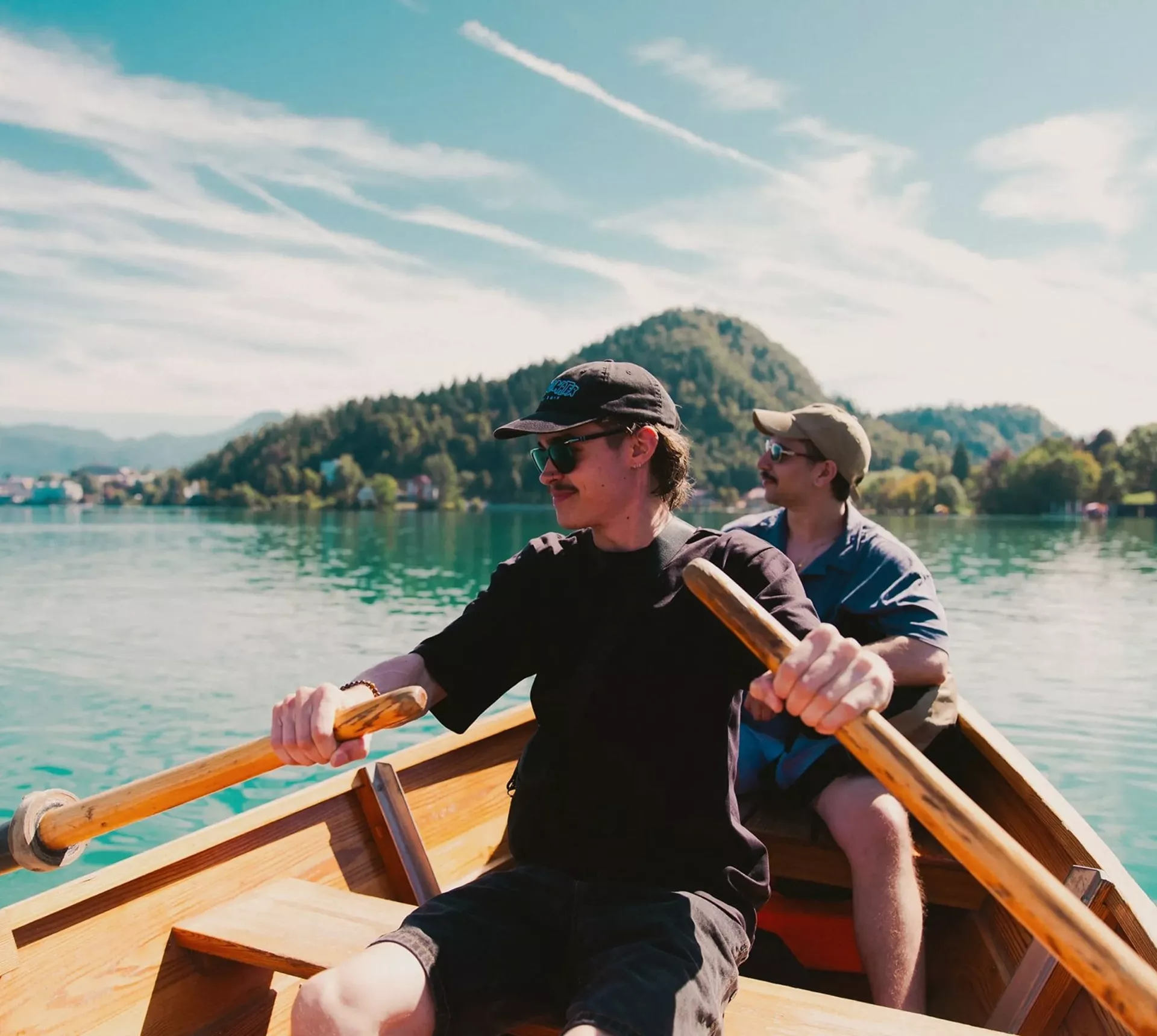 Travellers take in stunning mountain views while rowing across an emerald lake on the Contiki Budapest to Dubrovnik Tour