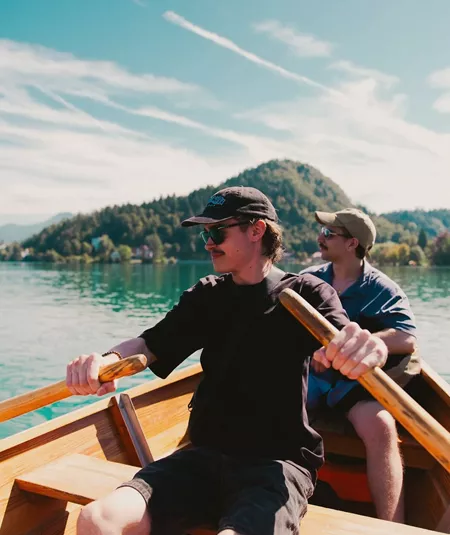 Travellers take in stunning mountain views while rowing across an emerald lake on the Contiki Budapest to Dubrovnik Tour